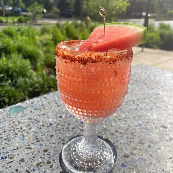 Watermelon margarita with a chili-lime rim and watermelon slice, on a speckled table outdoors.