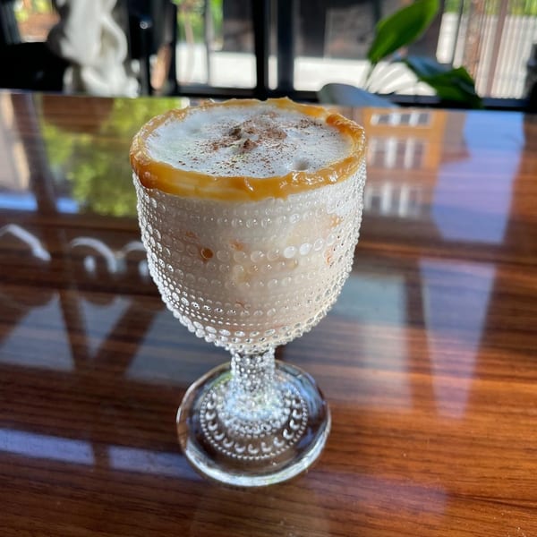A Mexican cocktail in a textured glass with a caramel rim, foam, and cinnamon on a wooden table.
