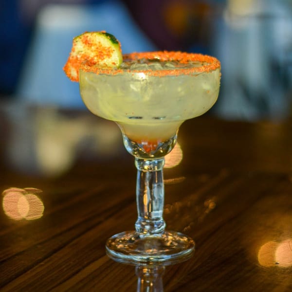 A margarita with a chili-lime rim and a lime wedge, on a wooden table.
